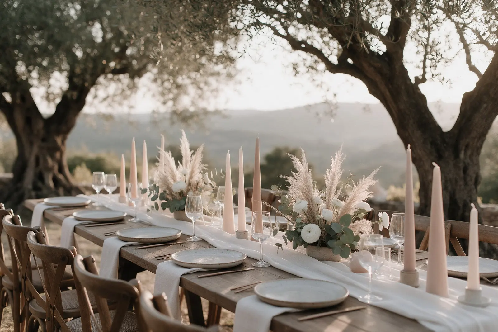 Longue table de mariage sous des oliviers en Provence, chemin de table en lin ivoire, bougies rose poudré et pampas