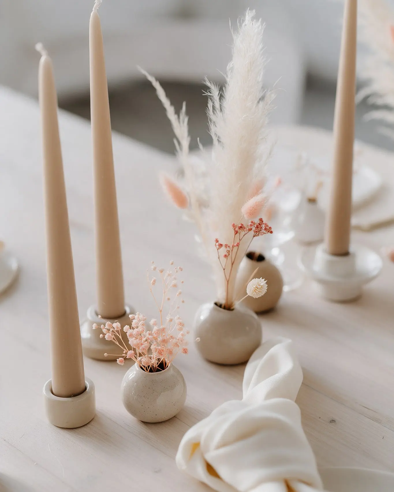 Bougies couleur sable, petits vases en céramique et pampas sur une table en bois clair