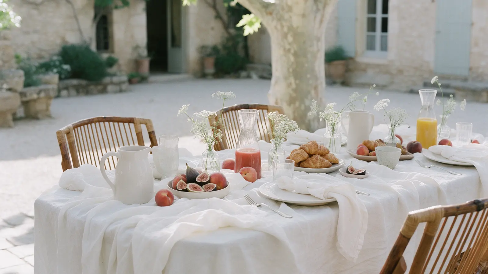 Table du brunch du lendemain dans une cour provençale : nappe de lin, figues, croissants et fleurs des champs