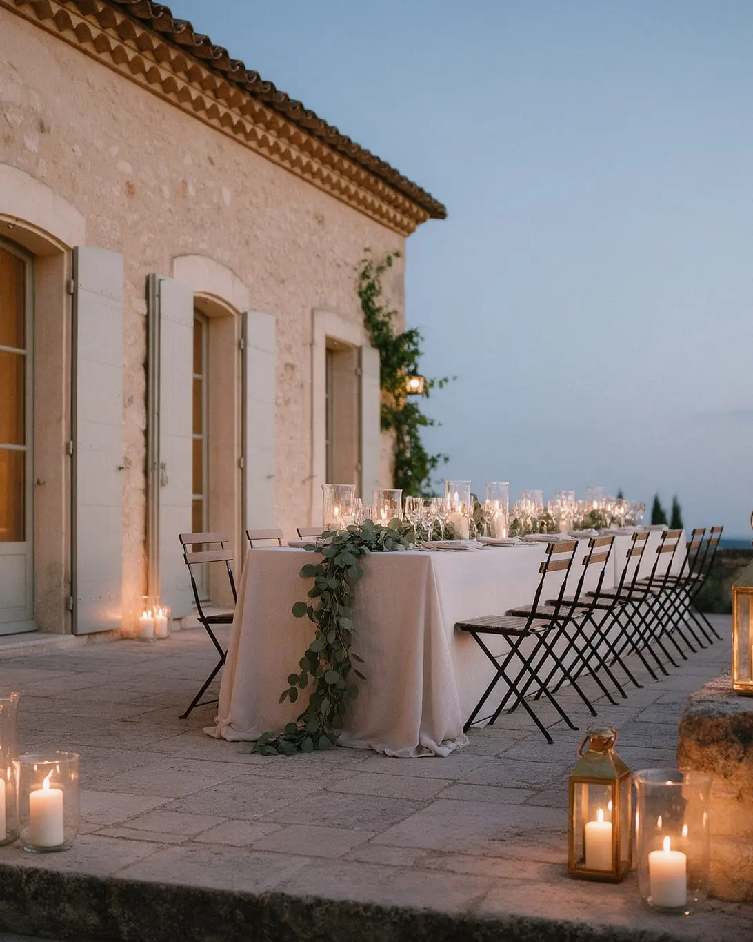 Terrasse en pierre d’une bastide au crépuscule, longue table dressée, bougies et lanternes